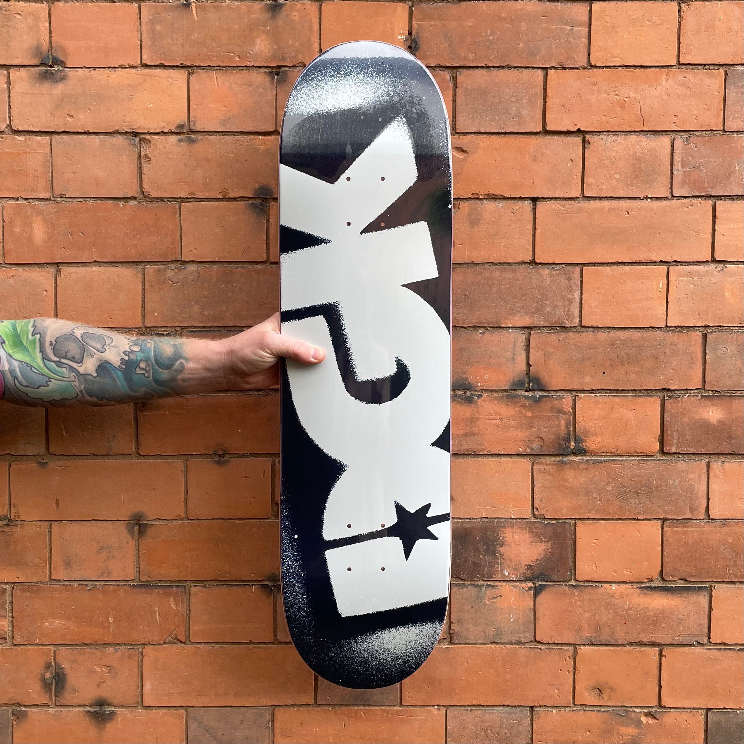 dgk skateboard held by a tattooed arm against a brick wall