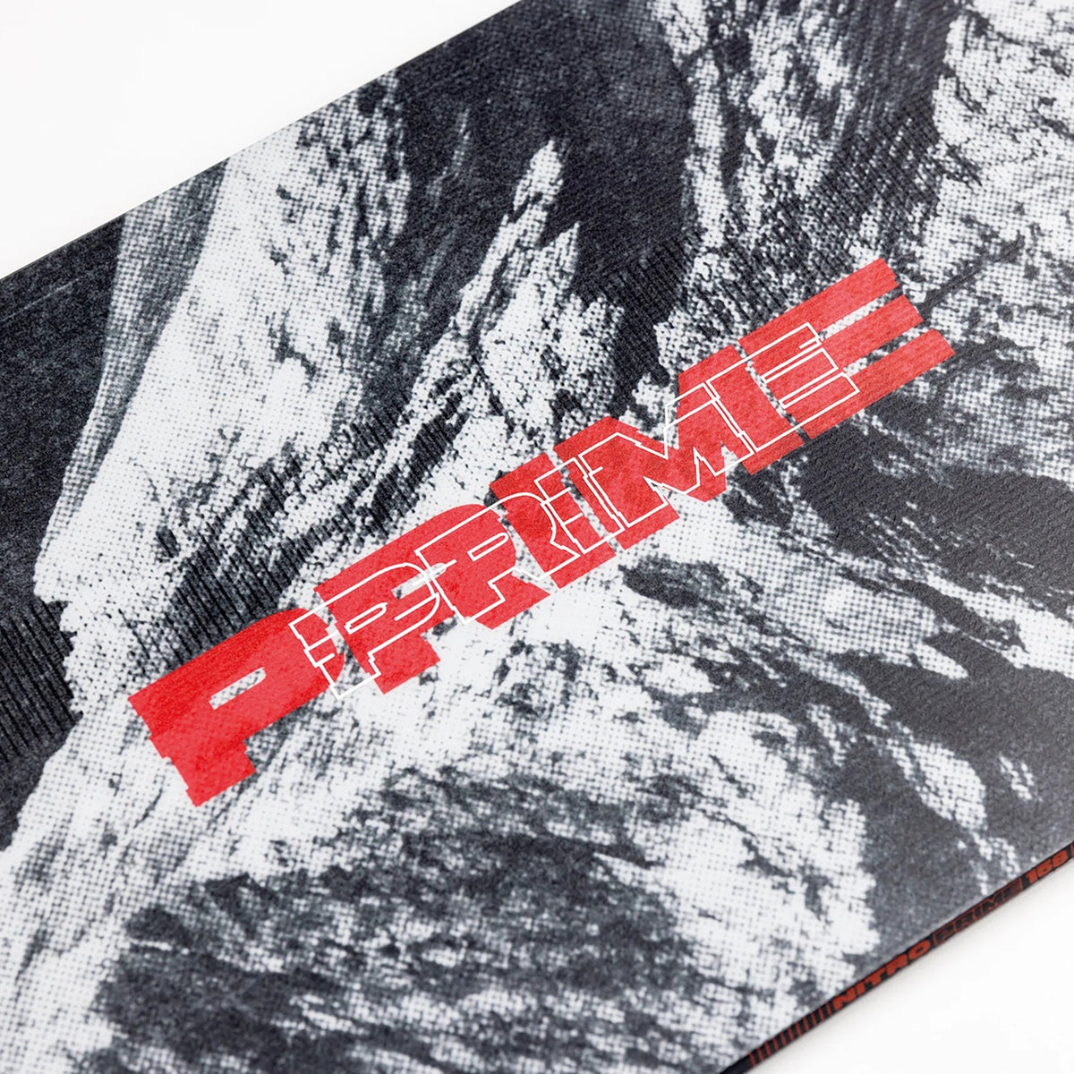 Close-up of a snowboard with a red PRIME logo on a mountainous background
