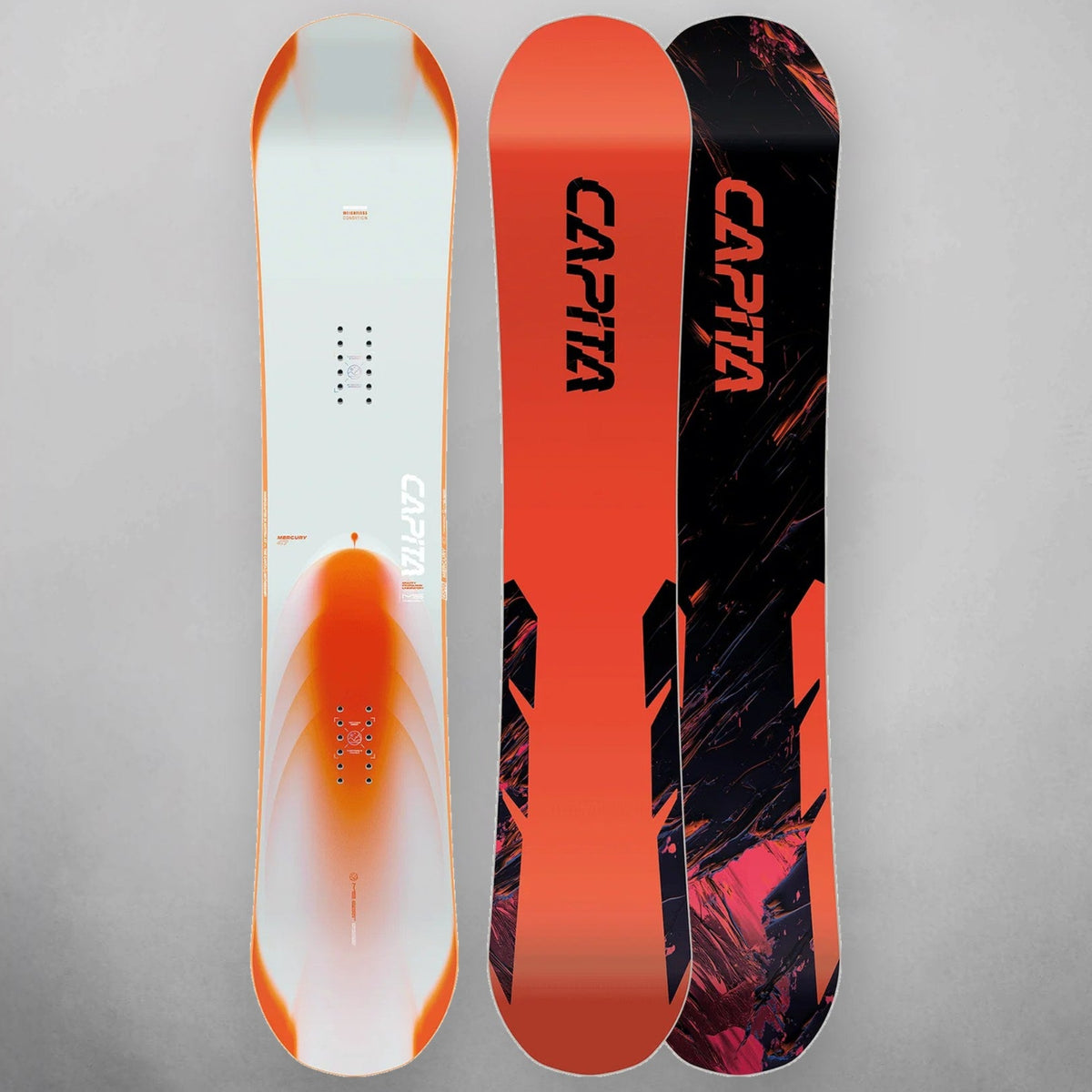 Three CAPiTA snowboards shown upright against a light gray studio background, displaying both the base and side graphics. The boards feature white, orange, black, and pink graphic designs with the CAPiTA brand name prominently printed on the sides.