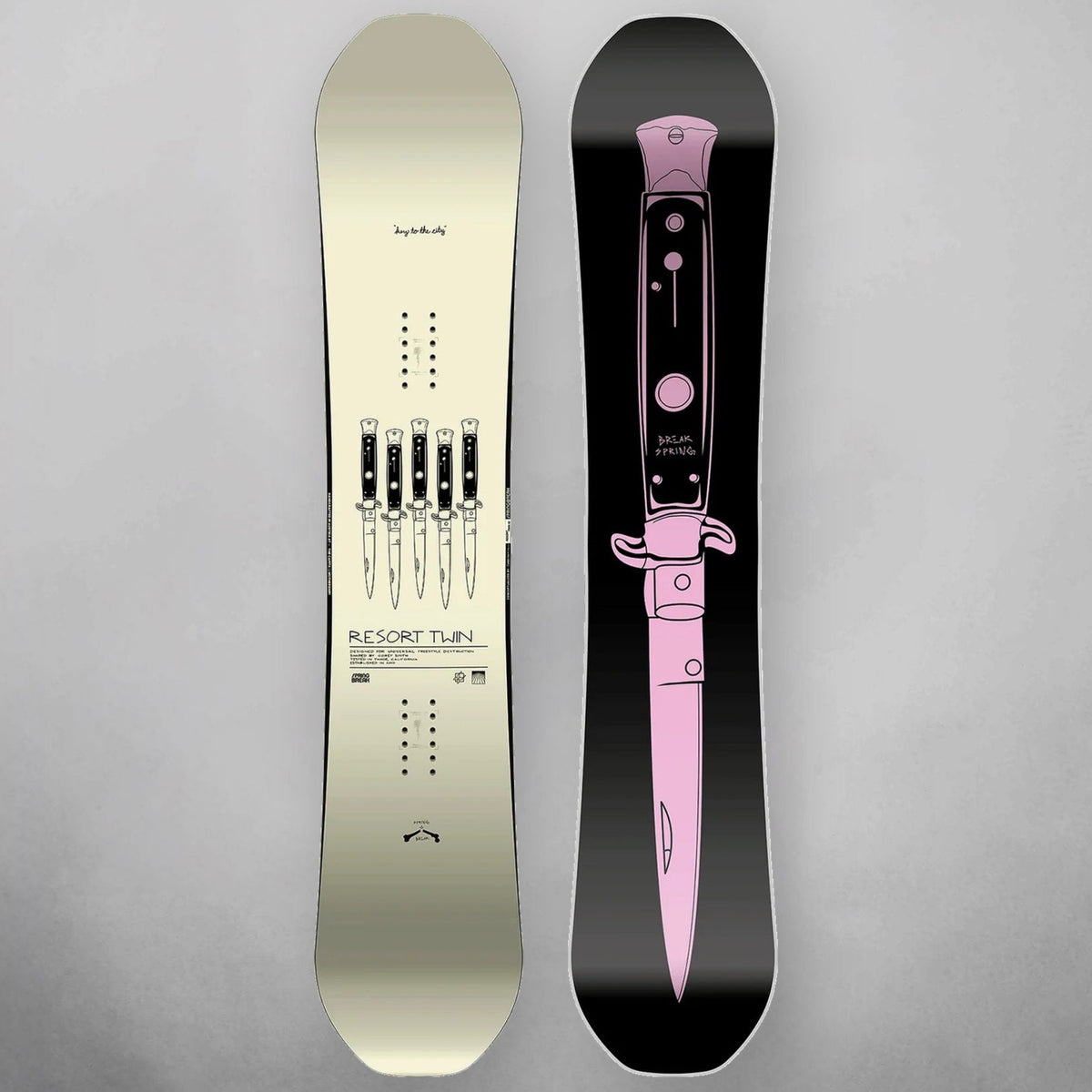 Two snowboard tops/views shown upright on a light gray background: one in warm off-white/cream with black bindings and printed text, and one in black with a large pink graphic and bindings visible.