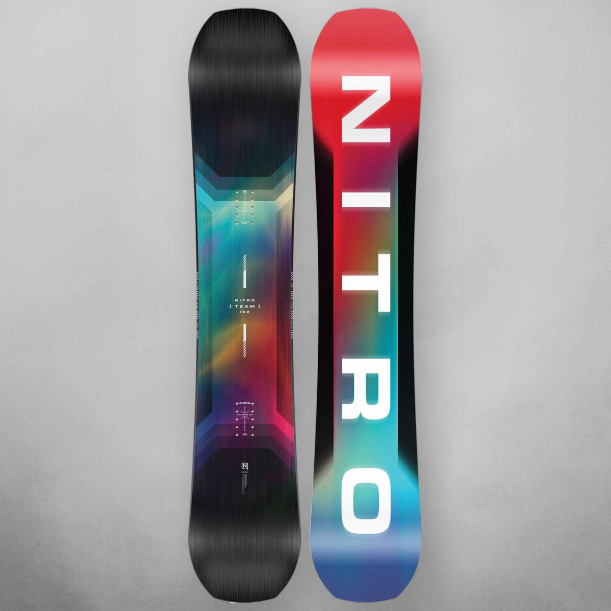 Two snowboards shown upright against a light gray background, displaying the topsheet designs. The left snowboard features a black base with a vibrant multicolor gradient of teal, pink, purple, and red.