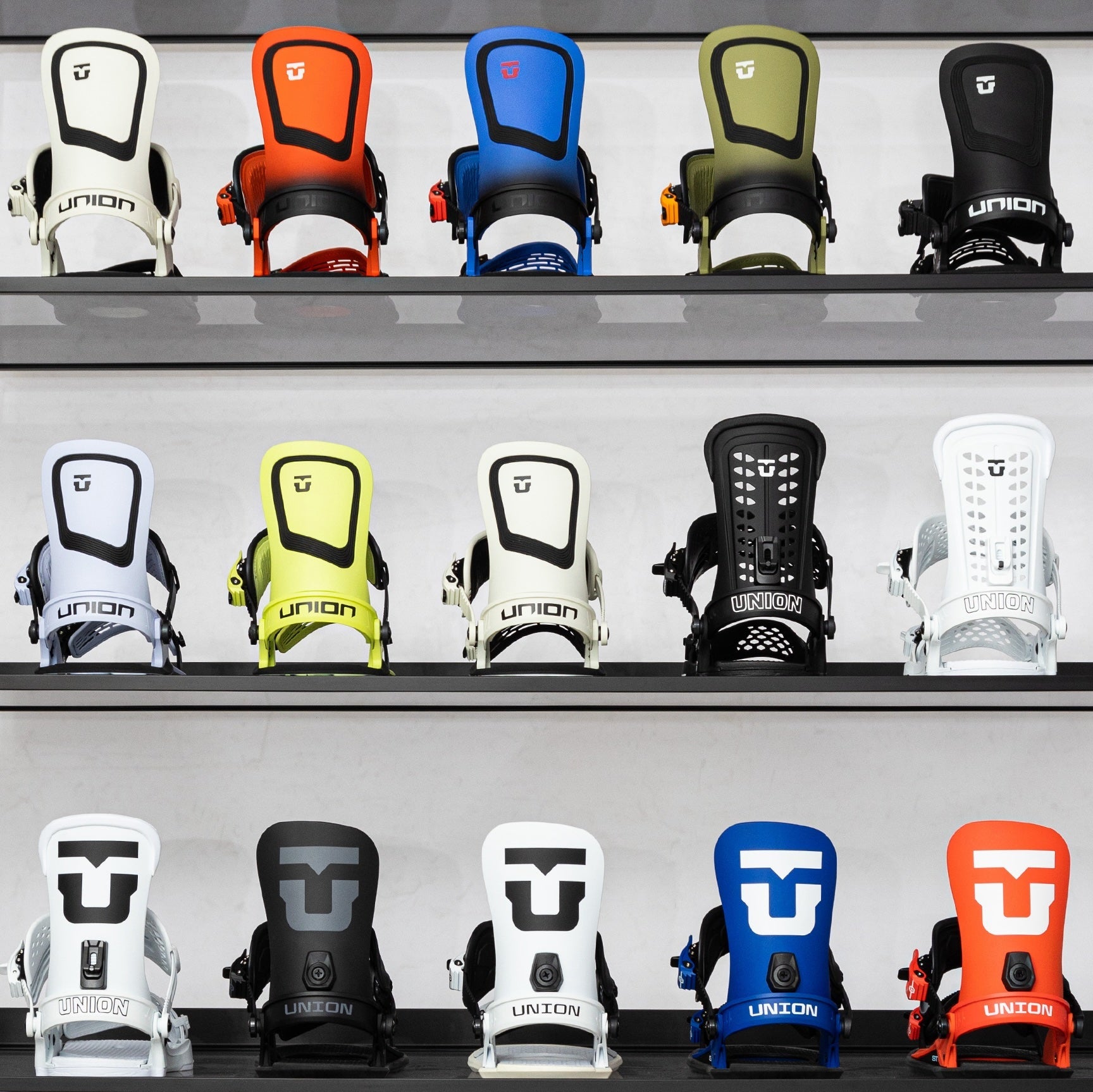 collection of snowboard bindings in a variety of bright colours on a white shelving unit