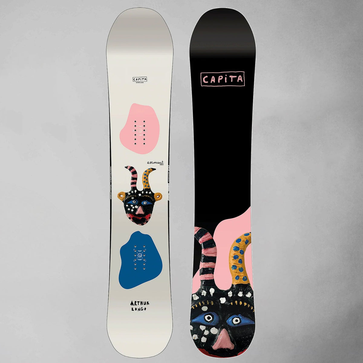 Two views of a snowboard on a neutral gray background: the white base showing pink, blue, and black graphic artwork, and the black base showing the matching artwork in reverse. The brand name CAPiTA is visible on the black base.