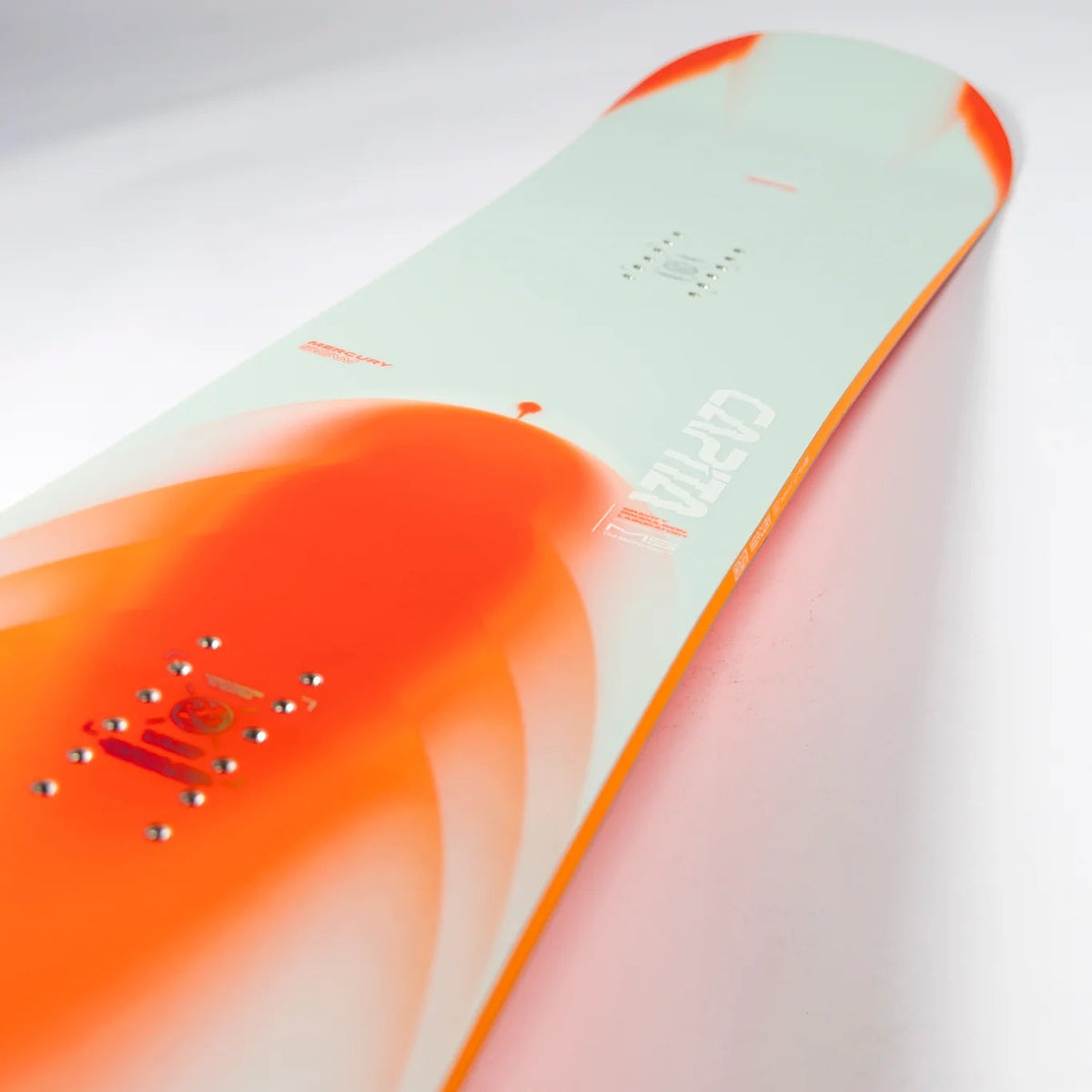 A close-up diagonal shot of a snowboard showing its top sheet in a pale mint green color with a large vibrant orange graphic and the brand name 'Cavalos' printed in white.