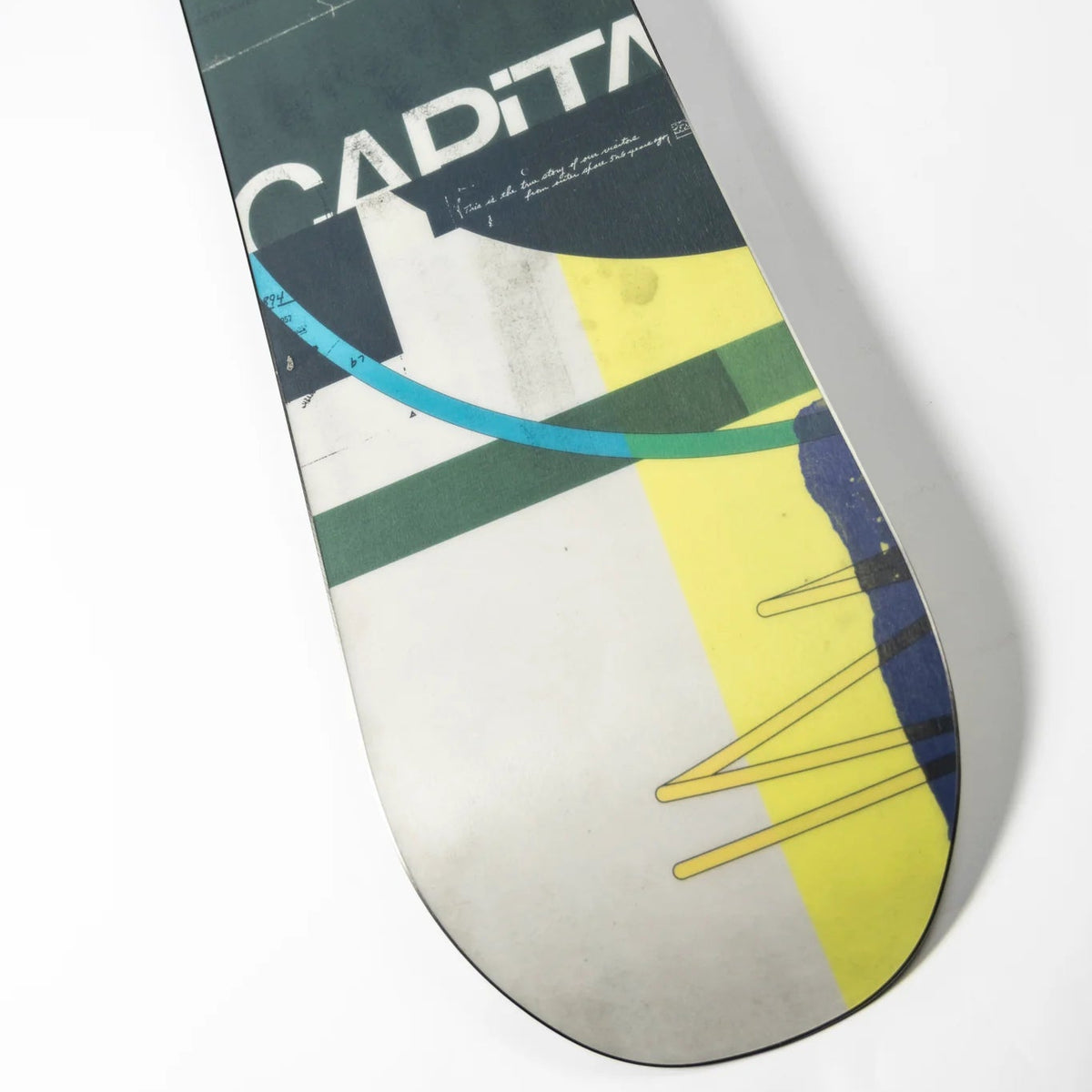 A close-up of a snowboard tail showing the brand name 'CAPiTA' in white over a dark green section, with abstract geometric patterns in yellow, teal, white, and dark blue on a white background.
