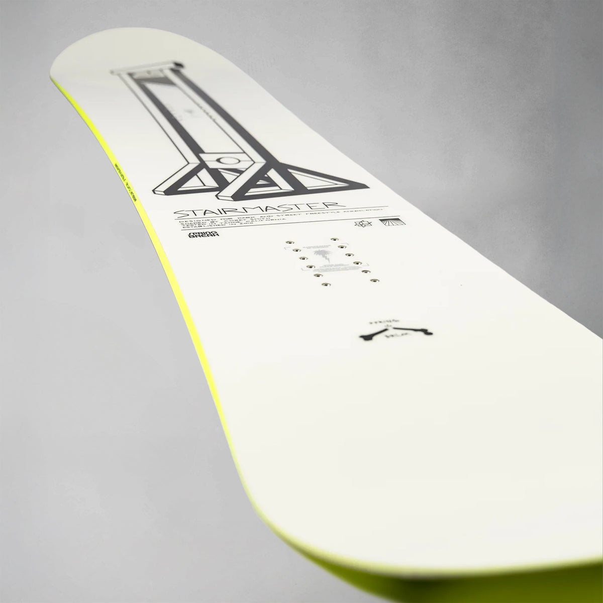 A close-up of a snowboard deck showing the underside, featuring a white base with a black graphic design, 'STAIRMASTER' text, and a bright neon yellow edge.
